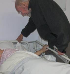 Elderly husband gazes at wife in hospital bed